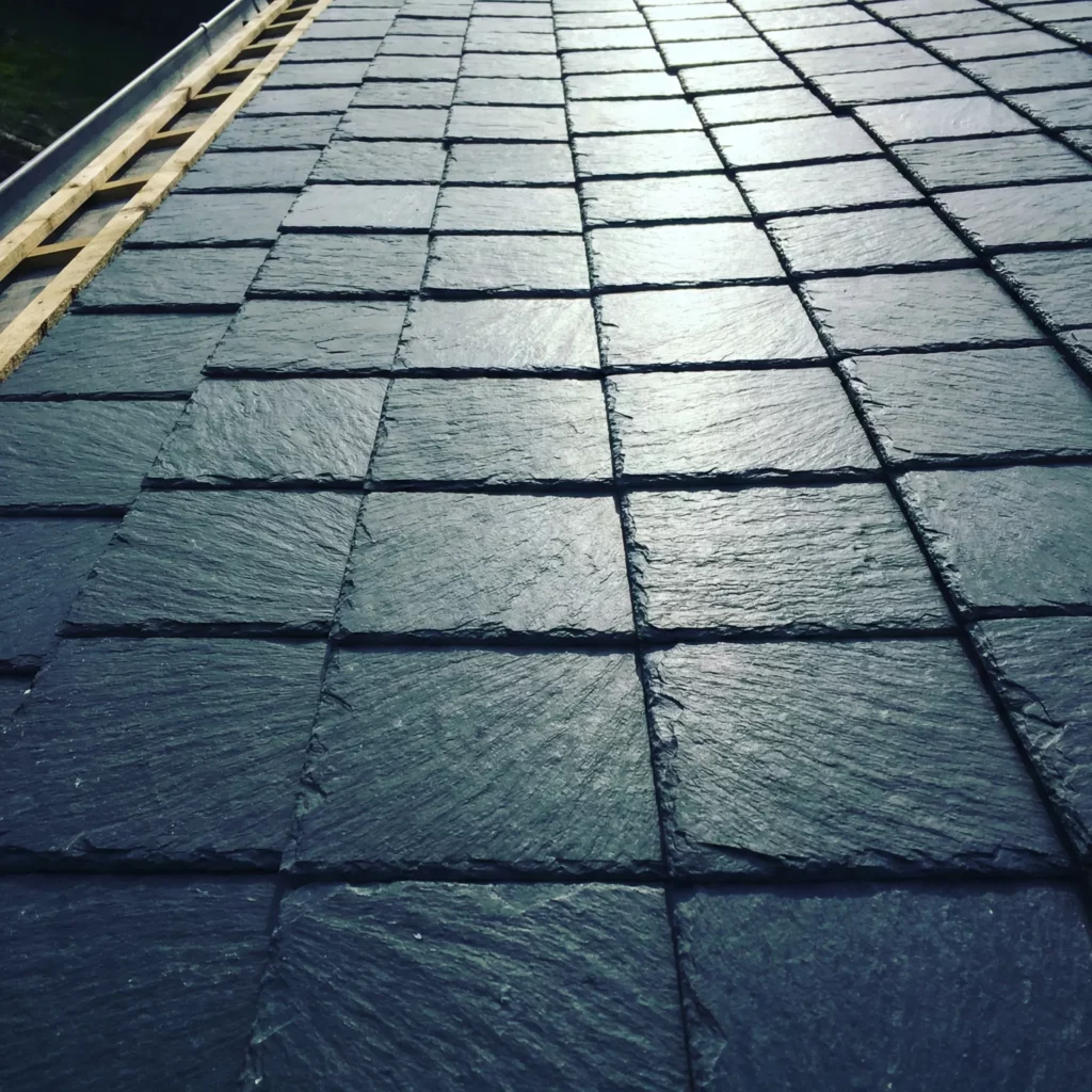 Gros plan détaillé d'une toiture en ardoises neuves, montrant la texture des tuiles sombres posées avec précision et les liteaux en bois visibles sur le bord.